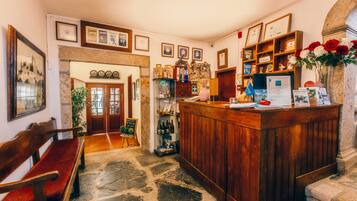 A reception area with a wooden counter, framed certificates, a welcome sign, and a vase with red and white flowers.