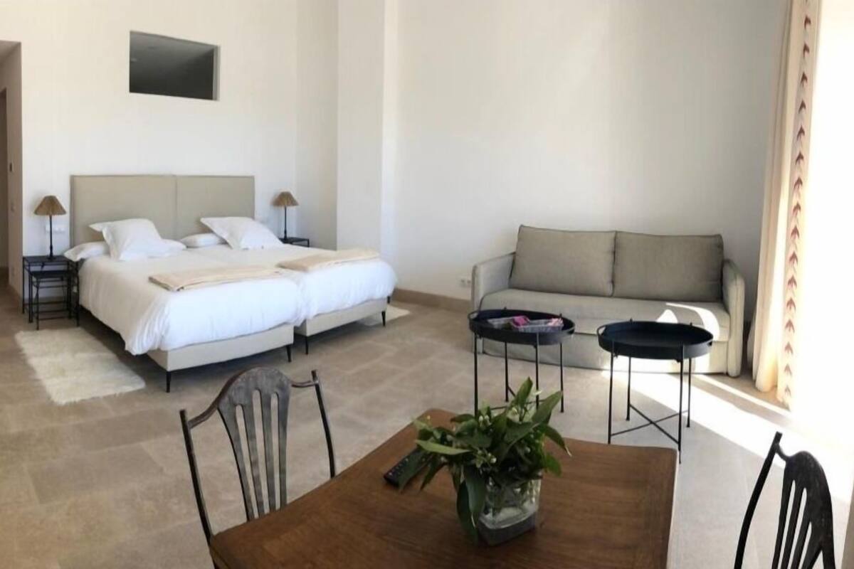 Ein Hotelzimmer mit einem Bett, einer Couch, einem Esstisch mit Stühlen und einer Topfpflanze.