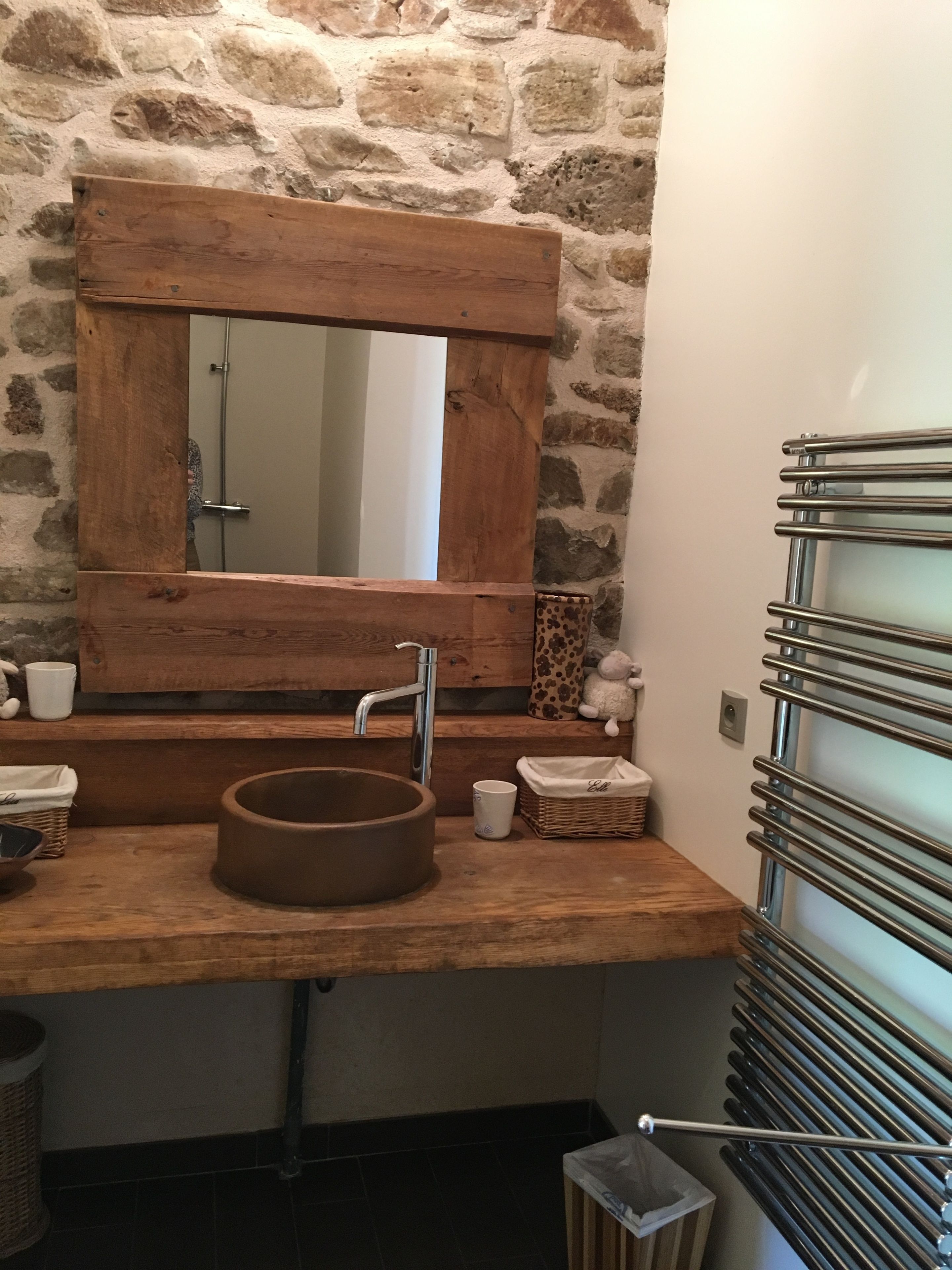 Une salle de bain avec un mur en pierre, un meuble-lavabo en bois, un lavabo rond et un porte-serviettes.
