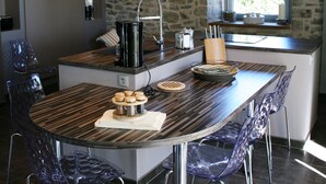 A modern kitchen with a central island, stone wall, and a large window. - La Bergerie Baroque (Verrieres)