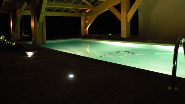 A nighttime swimming pool area with wooden beams and a covered roof. - La Bergerie Baroque (Verrieres)