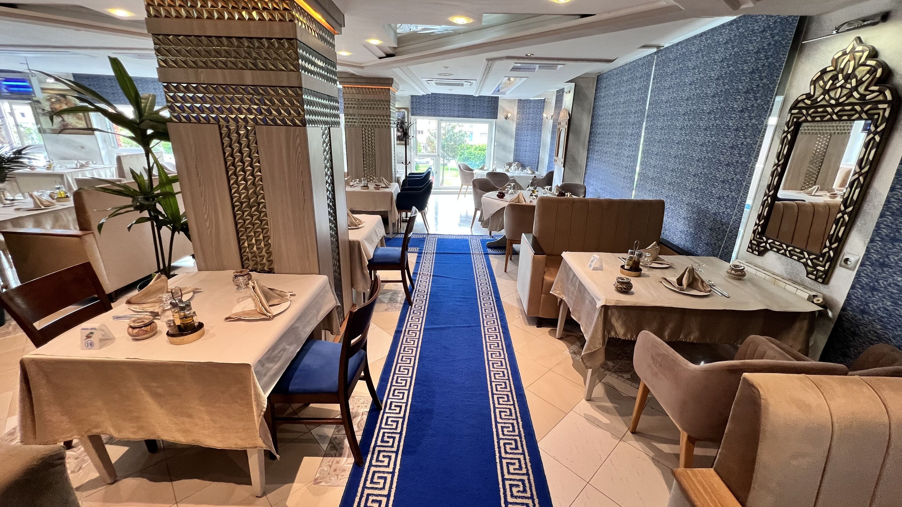 A restaurant with a blue patterned carpet leading to tables, wooden columns, and a large mirror on the wall.