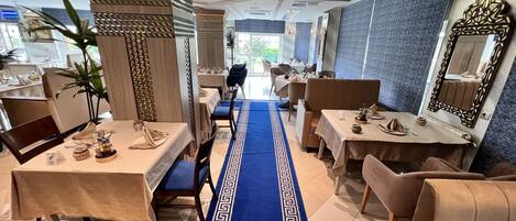 A restaurant with a blue patterned carpet leading to tables, wooden columns, and a large mirror on the wall.