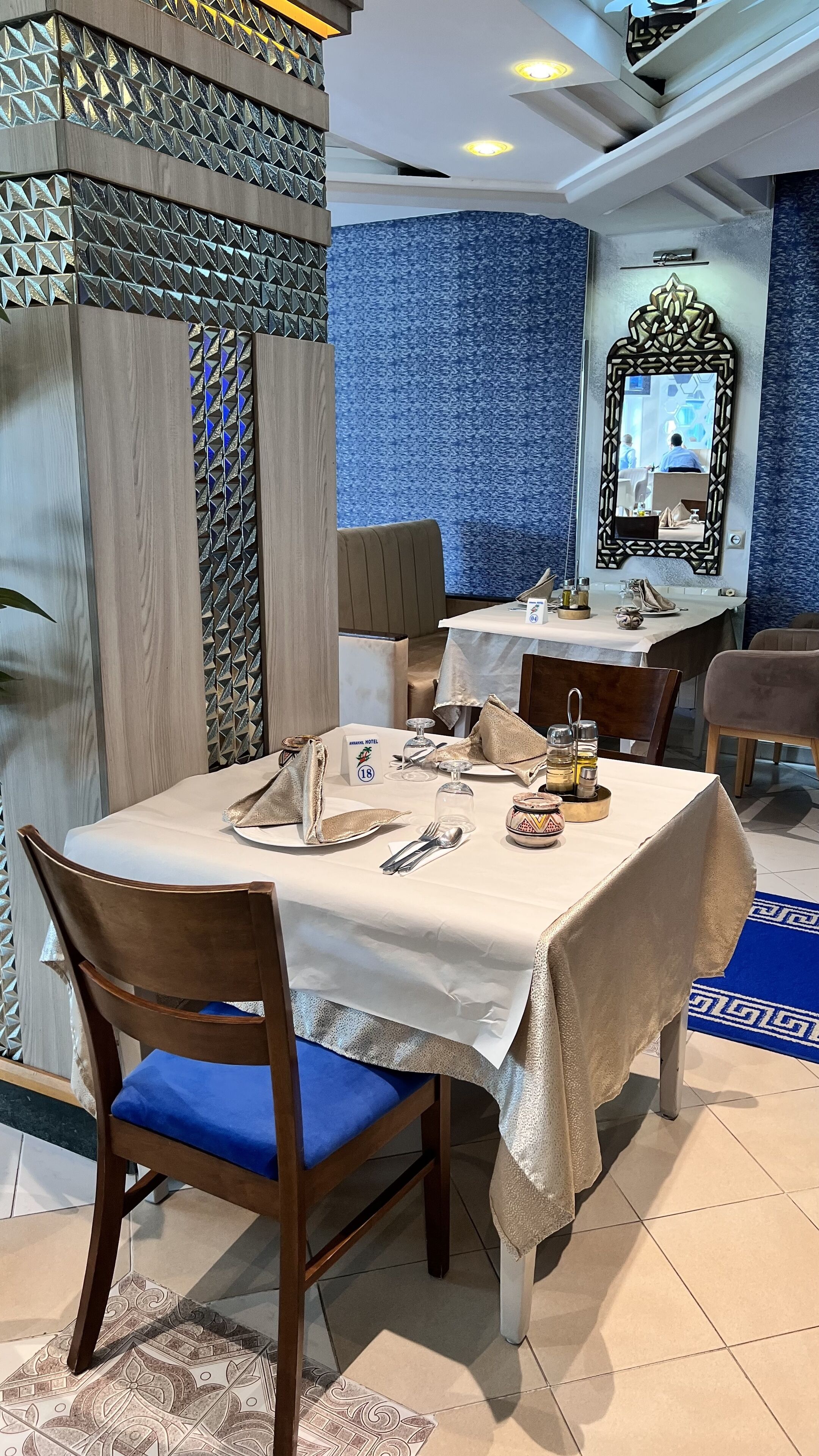 A dining area with a table set for two, a mirror, and a patterned wall.