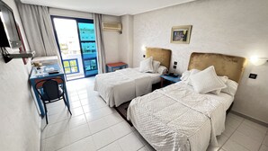 A hotel room with two beds, a desk, a chair, a small table, and a view of the outside.