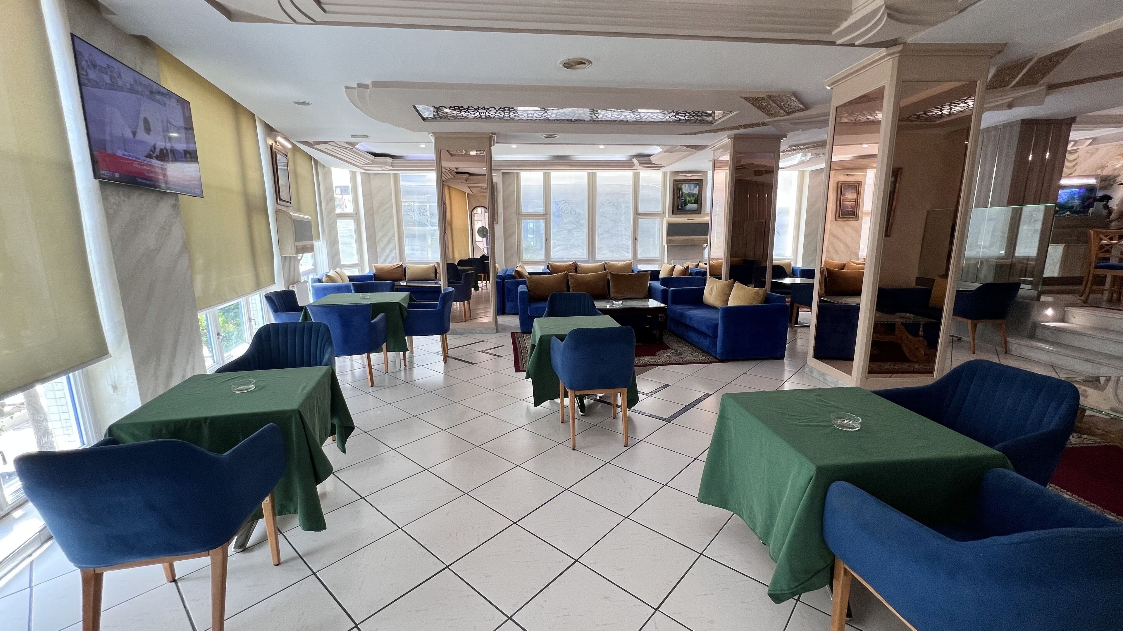 A restaurant with blue and green tables and chairs, large windows, and a tiled floor.