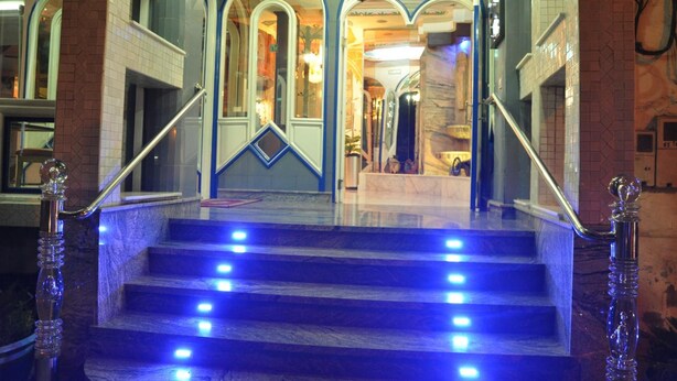 A grand staircase with blue lighting, ornate railings, and a chandelier.