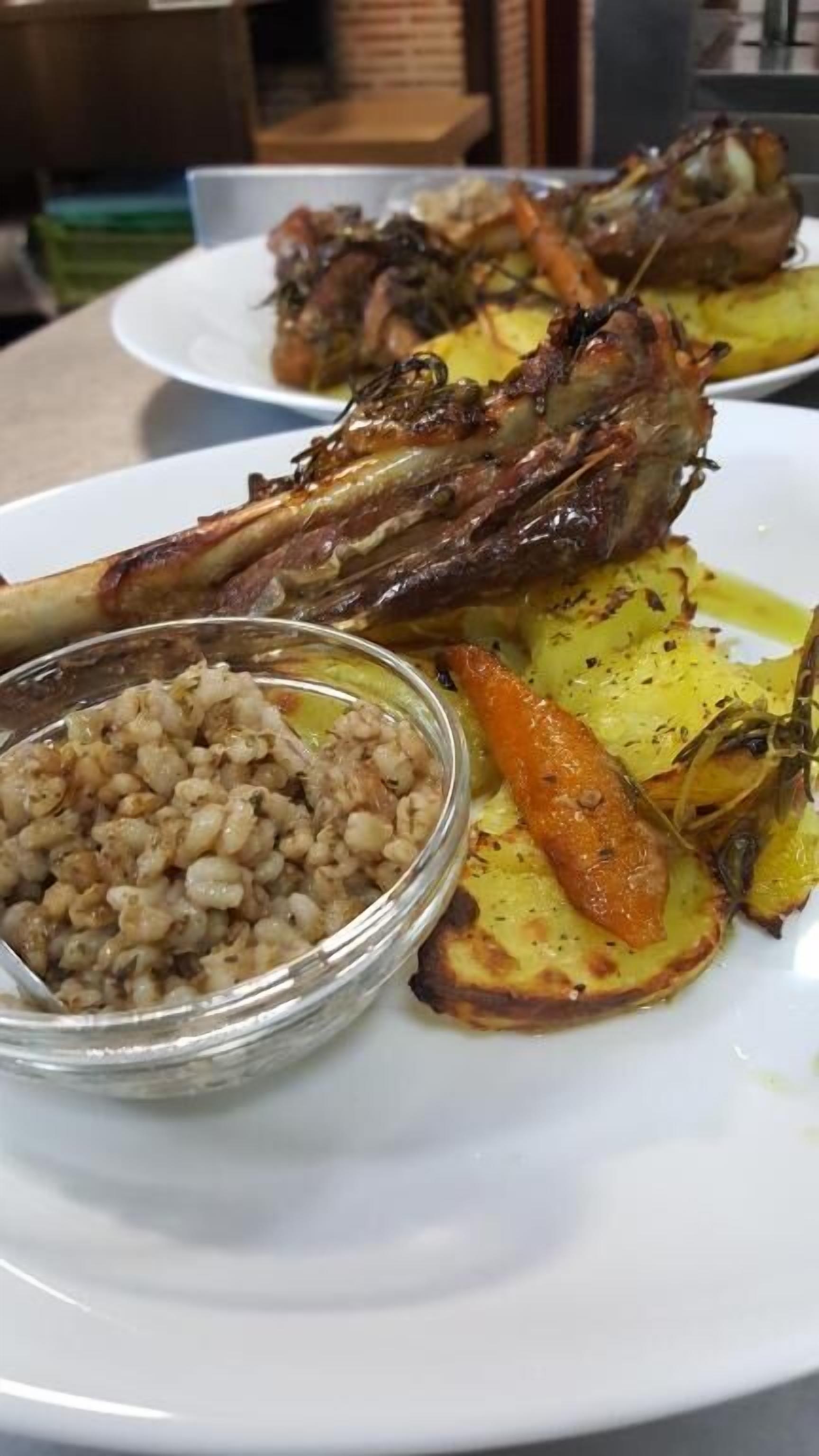 Une assiette contenant de l’agneau rôti, des pommes de terre rôties et un bol qui semble contenir un accompagnement à base de céréales.