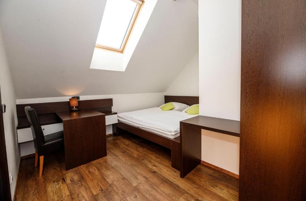 A small, modern bedroom with a skylight, a bed with green pillows, a desk, and a chair.