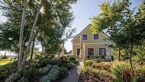 A two-story house with a paved pathway leading to the entrance, surrounded by lush greenery and trees. - Penzion Blanský Les (Kvítkovice)