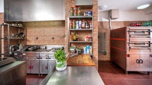 A commercial kitchen with stainless steel appliances, a brick wall, and a variety of food products on shelves. - Penzion Blanský Les (Kvítkovice)