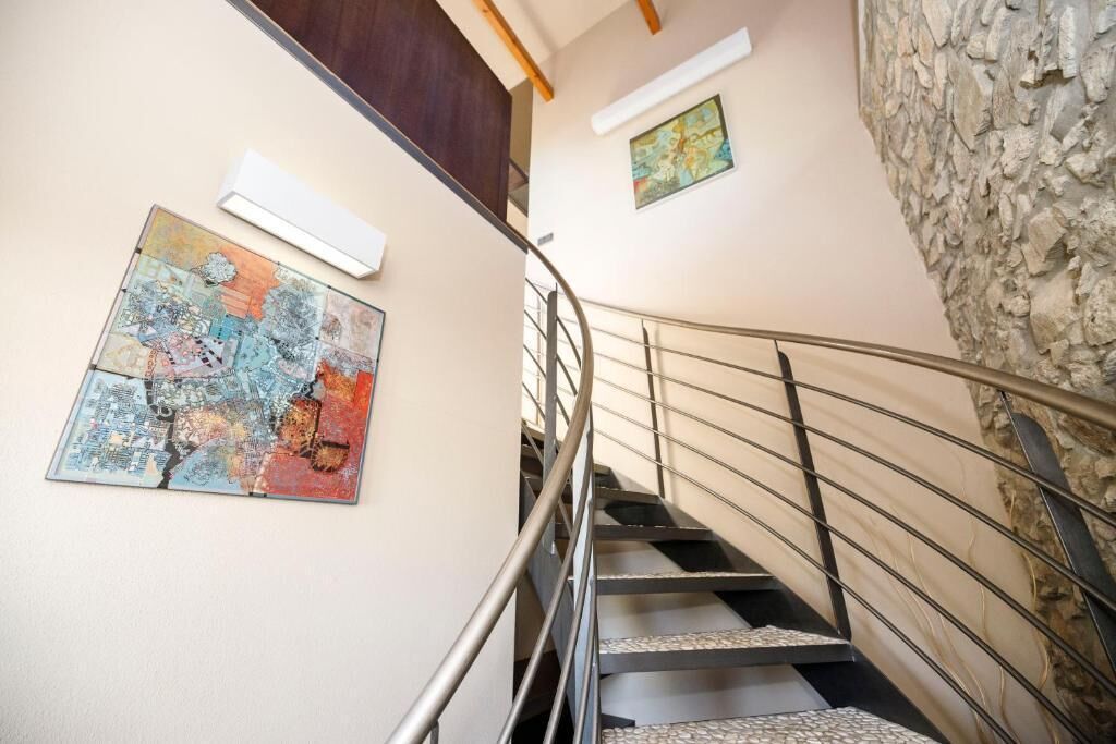 A spiral staircase with metal railings, a stone wall, and two artworks on the walls.
