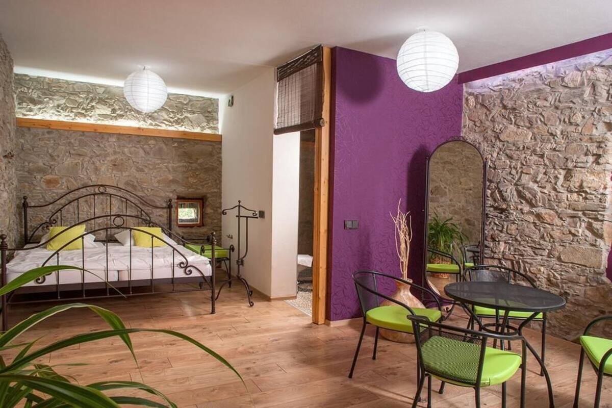 Quarto com parede de pedra, uma cama, parede de destaque roxa, área de refeições com cadeiras e uma mesa.