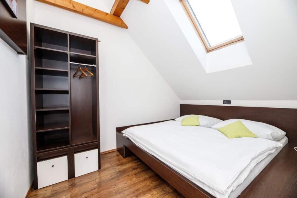 Quarto com cama de madeira, roupeiro embutido e claraboia.