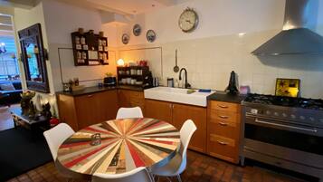 Une cuisine moderne avec une table ronde, des chaises blanches, des armoires en bois, une cuisinière et une horloge au mur.
