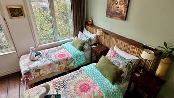 Une chambre avec deux lits, une fenêtre donnant sur un beau paysage, une horloge murale et un tableau représentant un Bouddha.