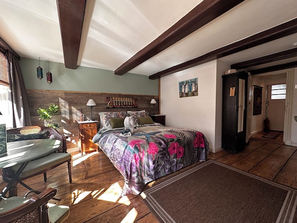 A bedroom with a wooden ceiling, a bed with a floral bedspread, a desk with a chair, and a small plant. - Amsterdam B&B Barangay (Amsterdam)