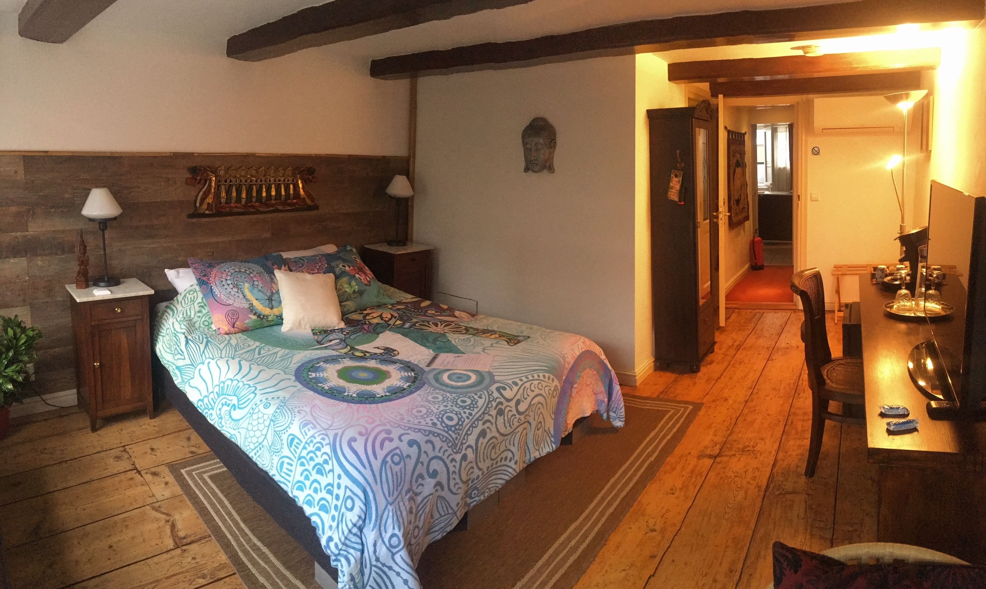 A bedroom with a bed, bedside tables, a lamp, a Buddha statue, and a dining area with a table and chairs.
