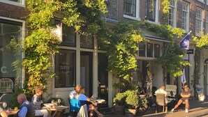 An outdoor café with tables and chairs, surrounded by greenery and buildings. - Amsterdam B&B Barangay (Amsterdam)