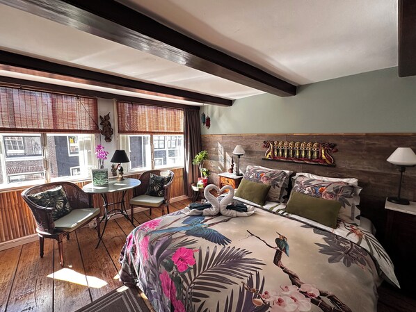 A hotel room with a bed, two chairs, a small table, and a window with a view of buildings. - Amsterdam B&B Barangay (Amsterdam)