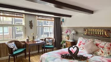 Relax in a spacious room with a large bed, floral bedspread, and a heart-shaped towel arrangement. Enjoy a dining table and chairs, plus a side table with a lamp.
