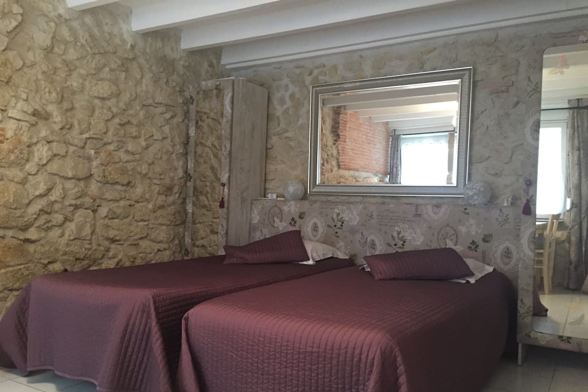 A room with two beds, a stone wall, a mirror, and a window with a brick wall behind it.