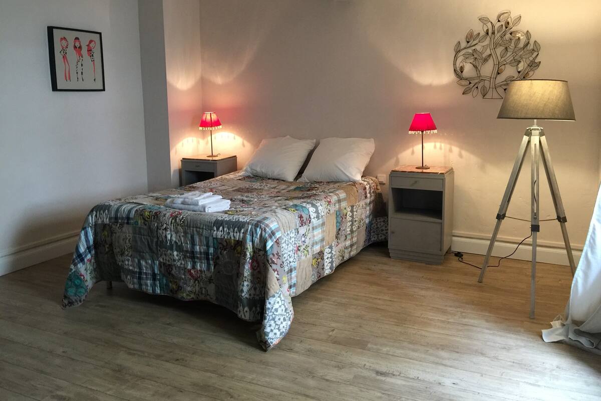 A bedroom with a bed, two bedside tables with lamps, a floor lamp, a wall decoration, and a framed picture.