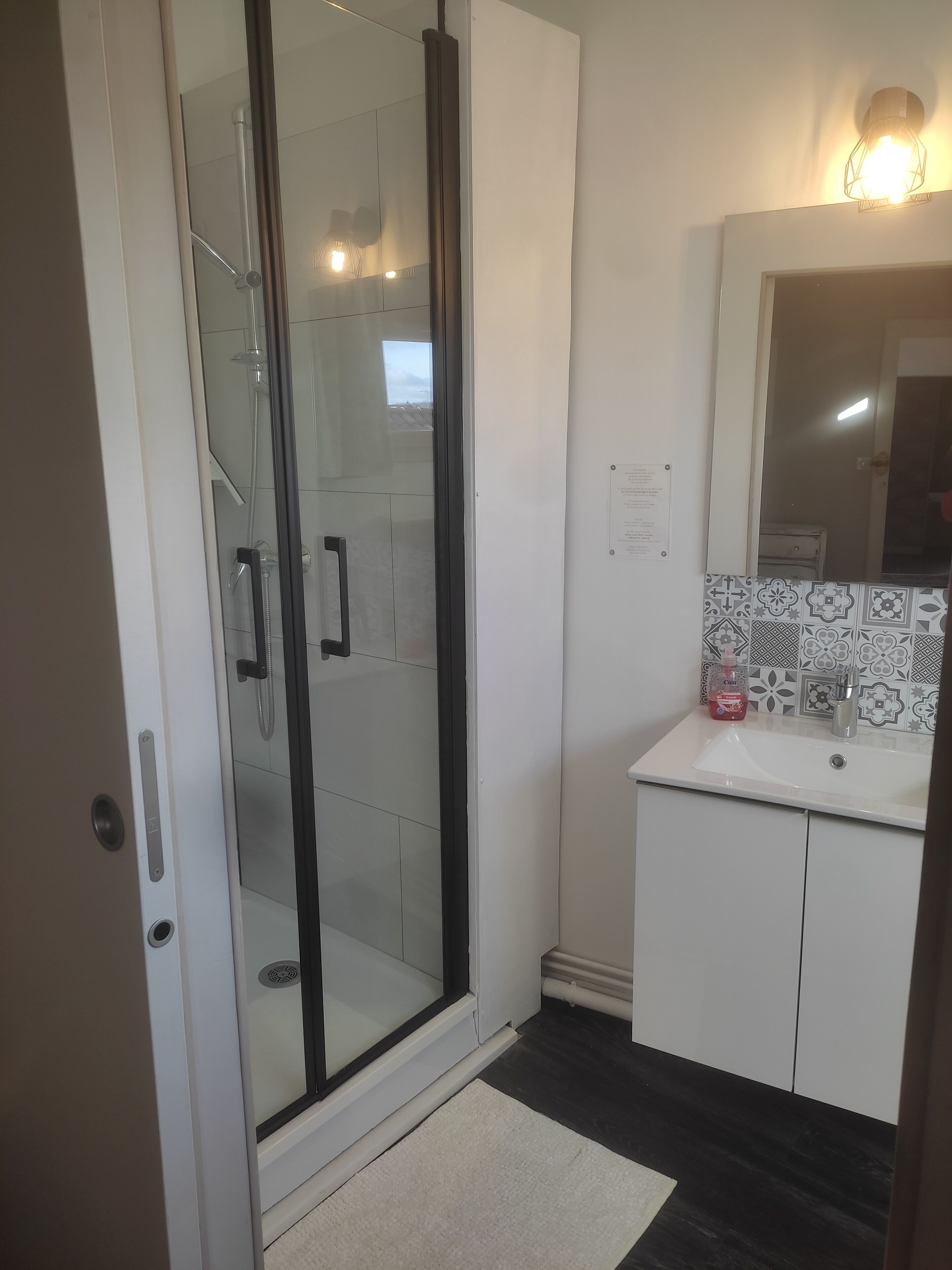 A modern bathroom with a glass shower enclosure, a white sink with a decorative tile backsplash, and a mirror above the sink.