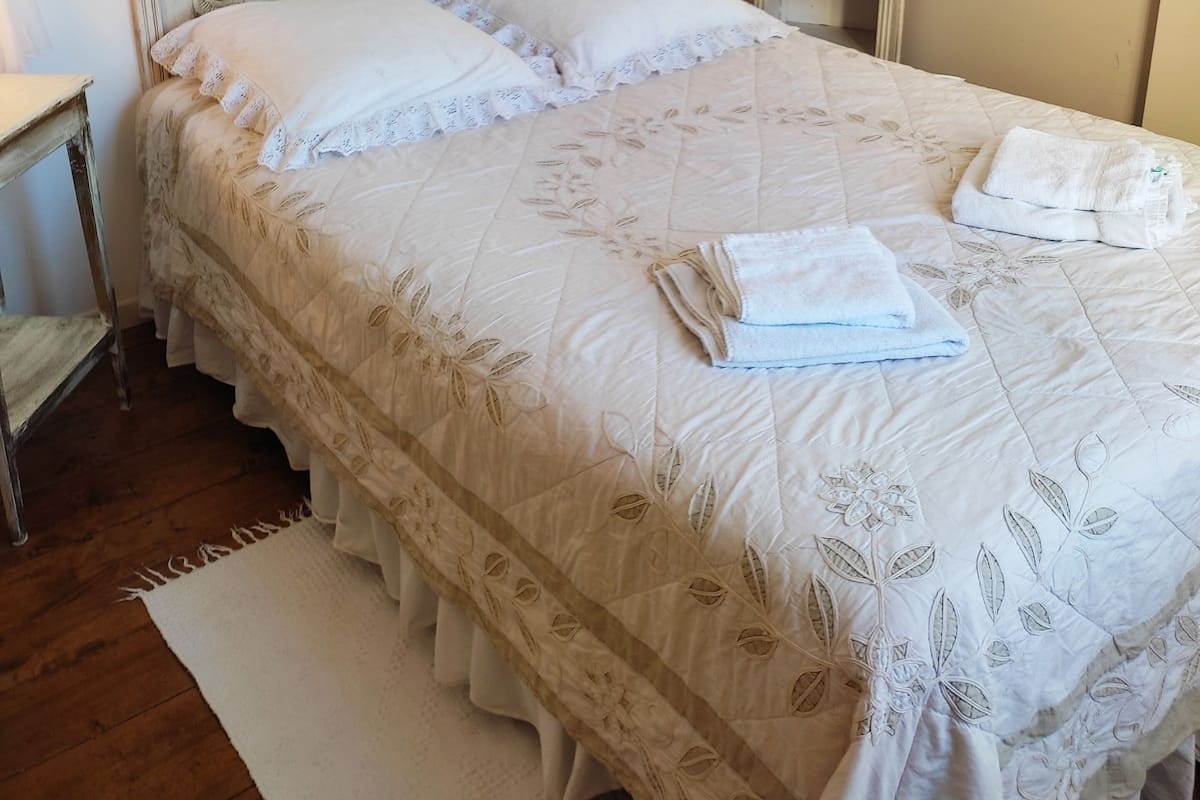 A bedroom with a bed, a bedside table, a nightstand, a lamp, and a window with curtains.