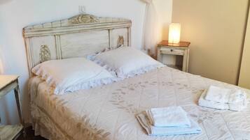 Un dormitorio con cama, mesita de noche, lámpara y ventana con cortinas.