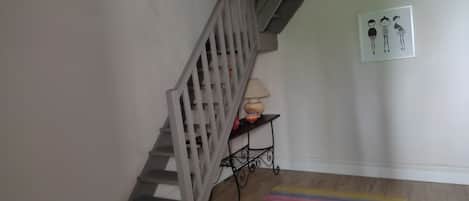 A staircase with a wooden handrail and a colorful striped rug at the bottom.