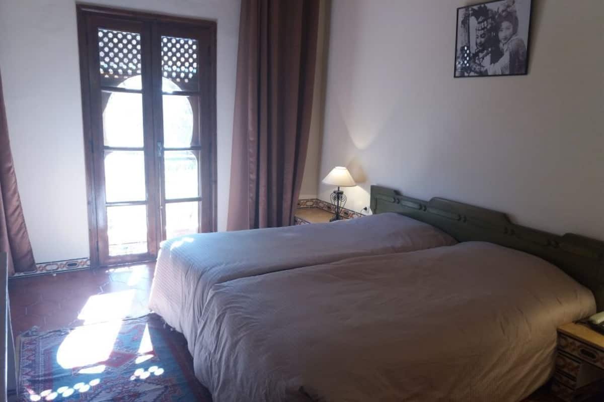 Une chambre d’hôtel avec deux lits, une fenêtre avec des rideaux, une table de chevet avec une lampe et un tableau encadré au mur.