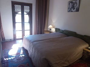 Ein Hotelzimmer mit zwei Betten, einem Fenster mit Vorhängen, einem Nachttisch mit Lampe und einem gerahmten Bild an der Wand.