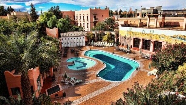 A resort with a large swimming pool, palm trees, and a courtyard with lounge chairs. - Hotel Club Hanane (Ouarzazate)