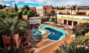 A resort with a large swimming pool, palm trees, and a courtyard with lounge chairs. - Hotel Club Hanane (Ouarzazate)