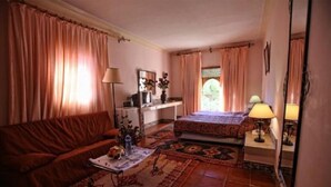 A cozy room with a sofa, a small table with a lamp, a bed, and a desk with a mirror. - Hotel Club Hanane (Ouarzazate)