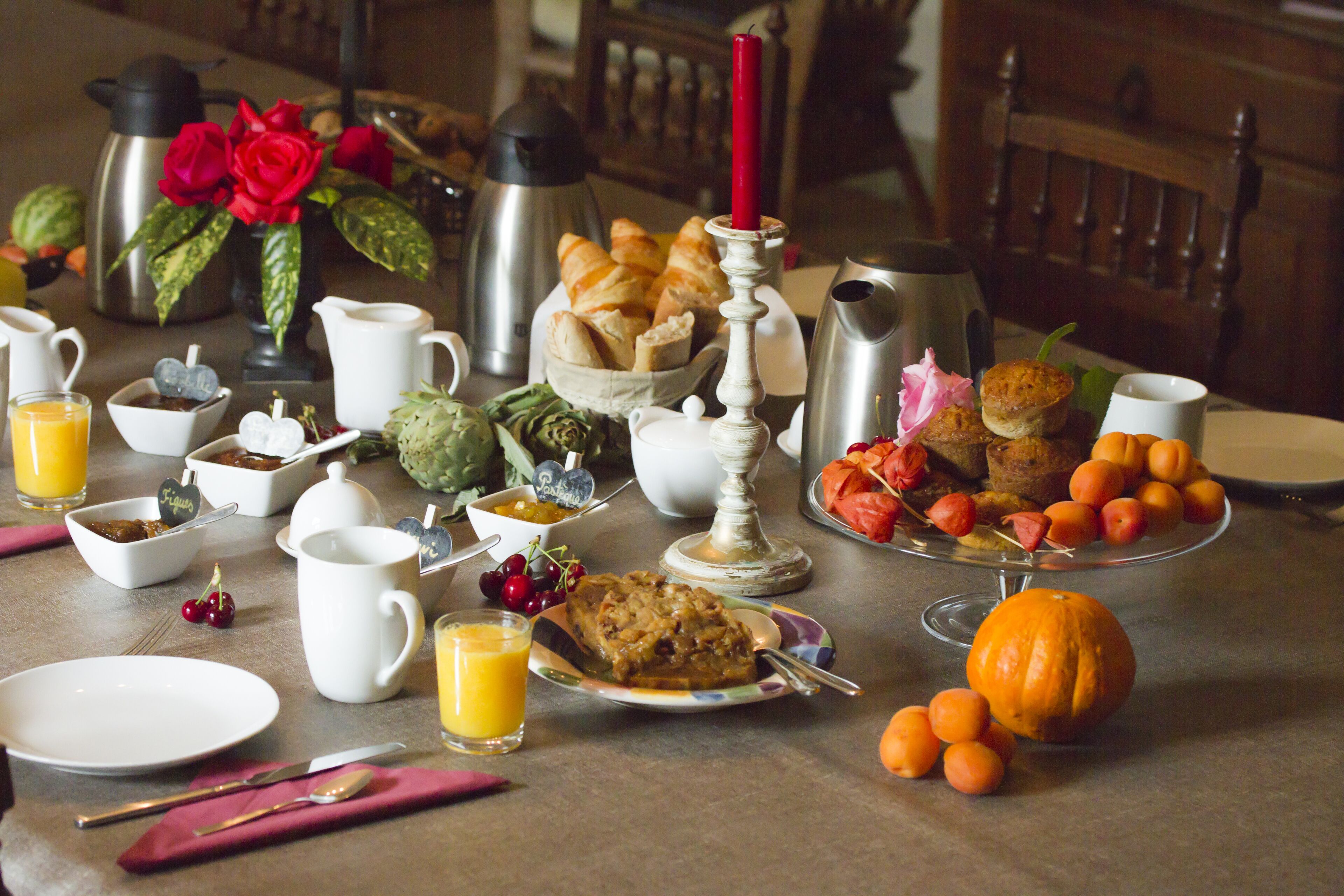 A breakfast table with various food items, a coffee pot, a thermos, and a candle.