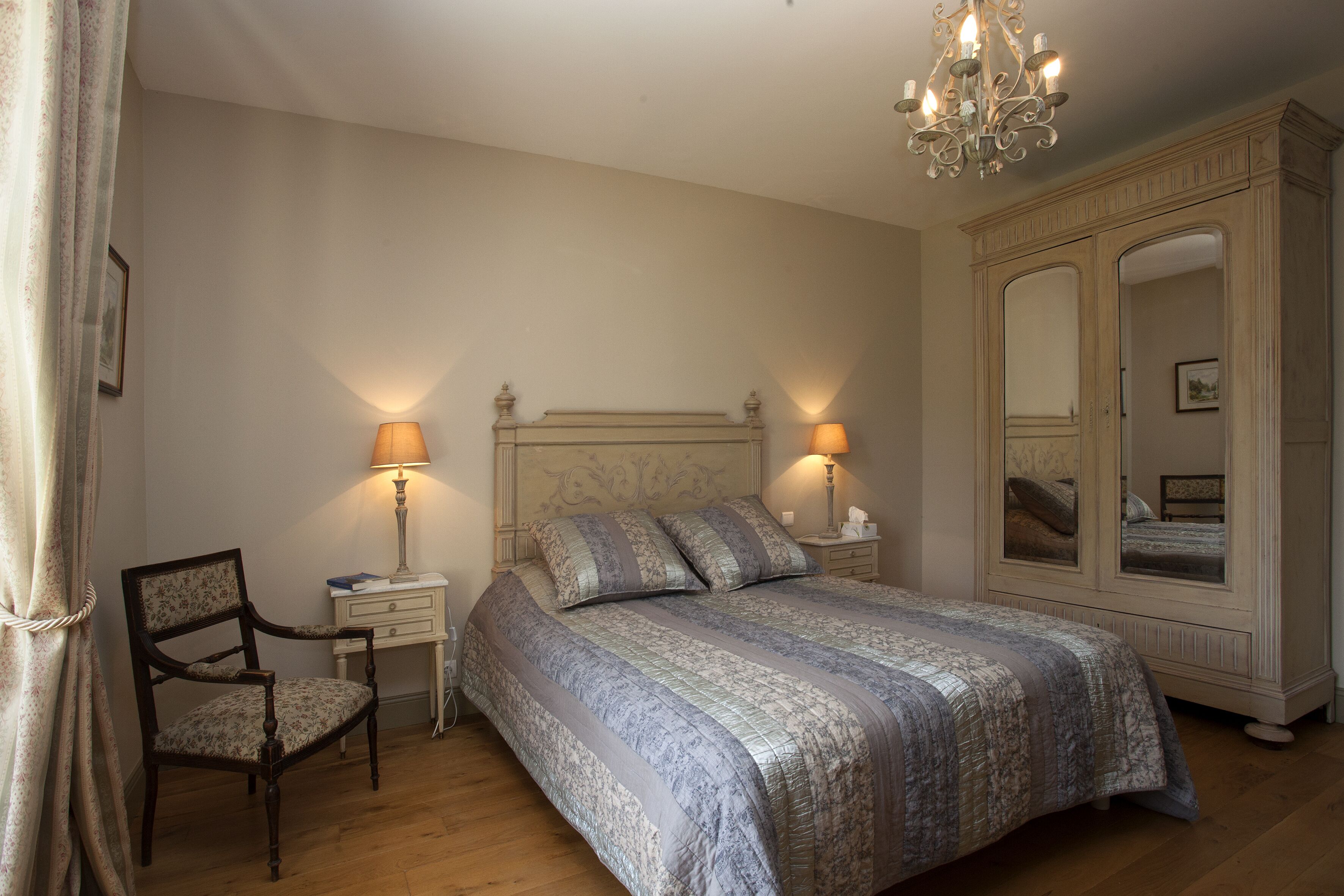 Quarto com uma cama grande, duas luminárias de cabeceira, uma cadeira, um guarda-roupa e um candelabro.