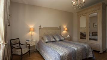 Quarto com uma cama grande, duas luminárias de cabeceira, uma cadeira, um guarda-roupa e um candelabro.