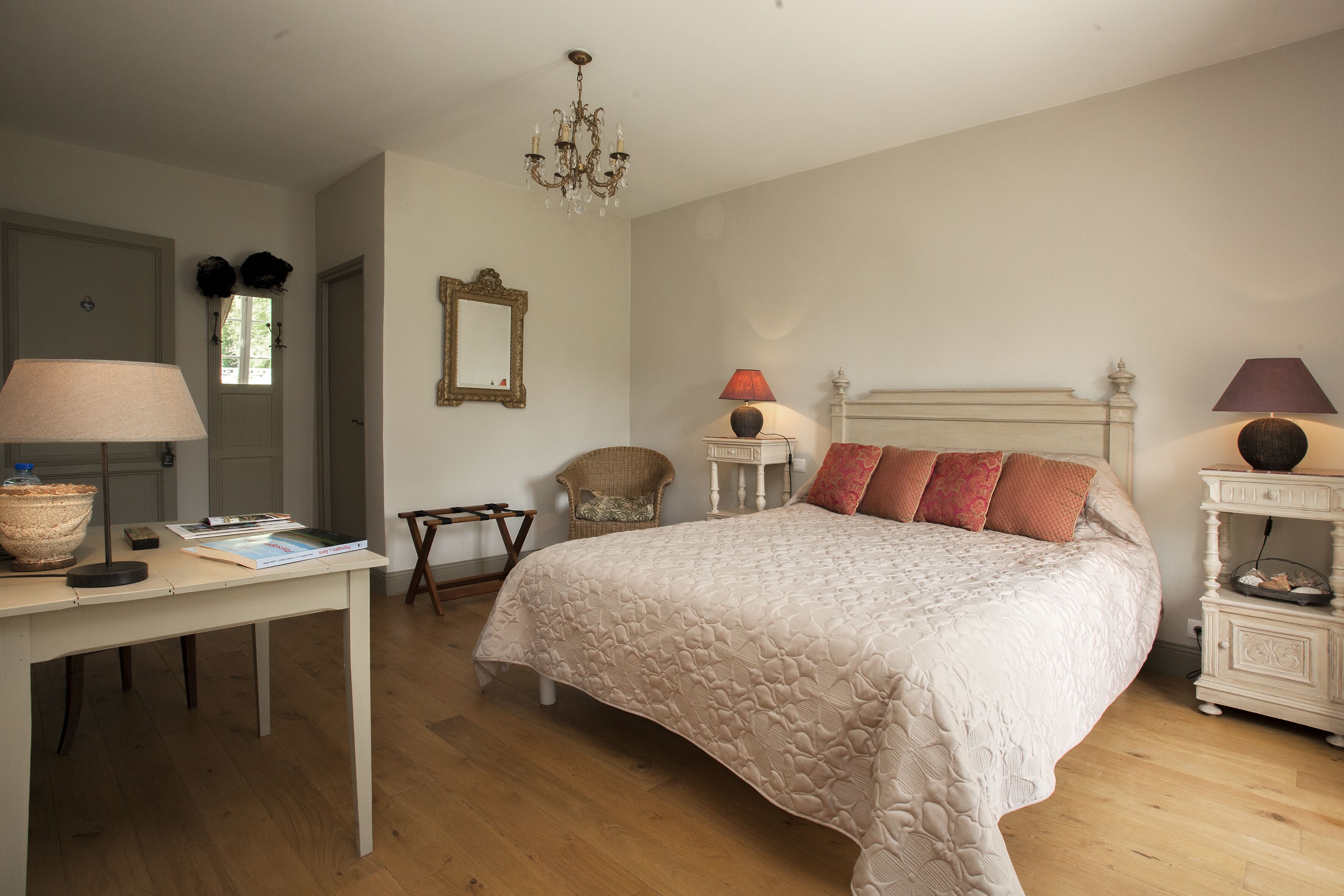 Een slaapkamer met een groot bed, een bureau met lamp, een stoel, een dressoir en een kroonluchter.