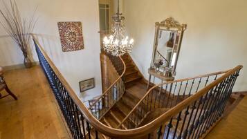 A grand staircase with a wooden handrail and black balusters, leading to a landing with a chandelier and a mirror.