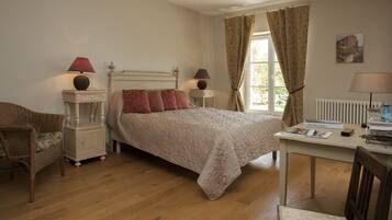 A bedroom with a bed, two bedside tables with lamps, a chair, a desk with a chair, and a window with curtains.
