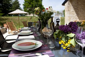 An outdoor dining table set with plates, glasses, and a bowl of soup. - Maison d'hotes de Charme Les Bruhasses (Condom)