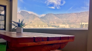 A wooden table with a potted plant on a balcony overlooking a mountainous landscape. - Cape Town Apartment with balcony (Cape Town)