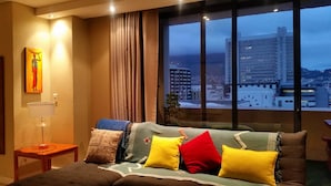 A hotel room with a large window, a bed with multiple pillows, a bedside table with a lamp, and a painting on the wall. - Cape Town Apartment with balcony (Cape Town)