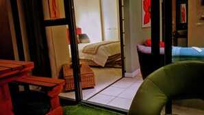 A room with a bed, a small table, a chair, and a glass door leading to another room. - Cape Town Apartment with balcony (Cape Town)
