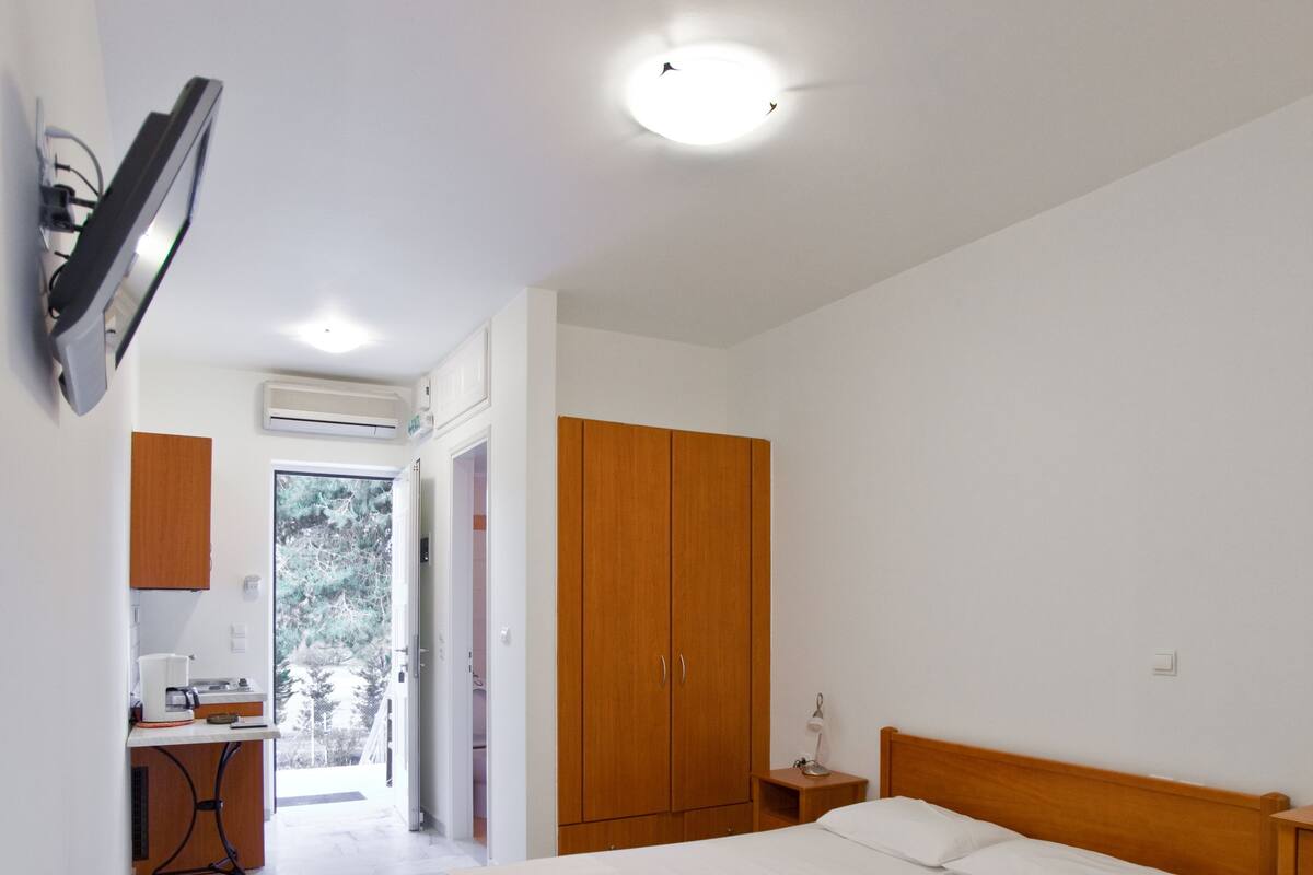 A bedroom with a wooden bed, a bedside table, a small desk with a chair, and a wardrobe.