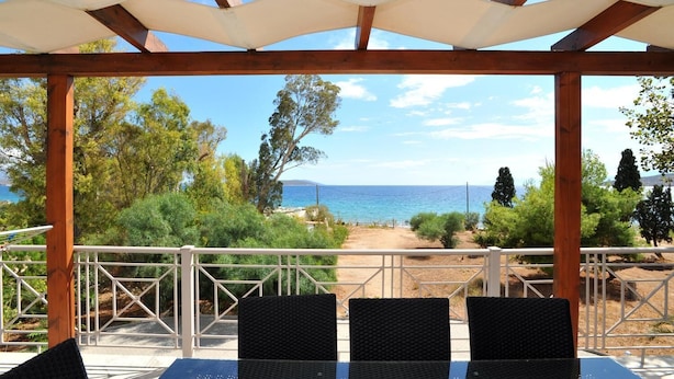 A covered outdoor seating area with a view of the sea and a dirt path leading to the beach. - Porto Assini (Nafplio)