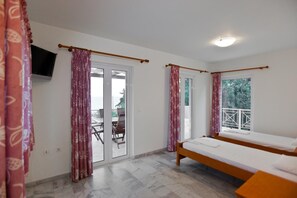 A bedroom with a bed, a TV, a balcony with a table and chairs, and a view of the sea. - Porto Assini (Nafplio)