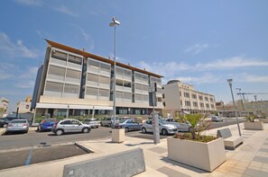 A modern building with multiple floors, a parking lot with several cars, and a clear sky. - Appartamento 5 Vele (Gallipoli)